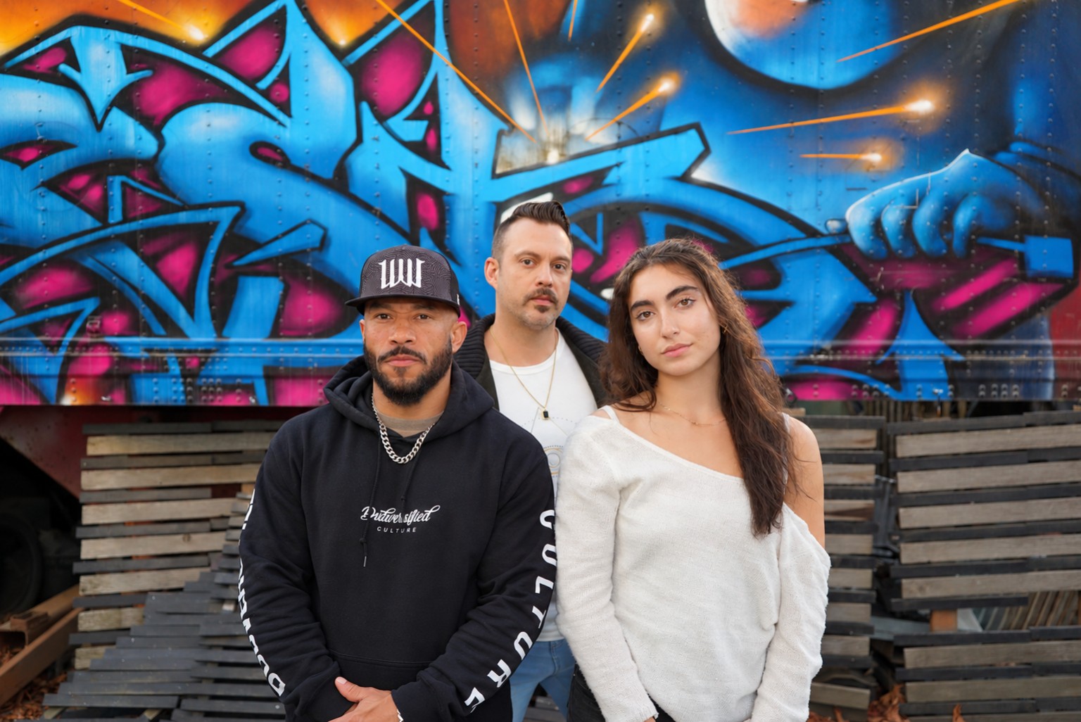 PSYOPS artist trio photographed in front of vibrant graffiti
